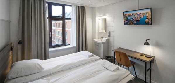 Habitación de hotel con cama, escritorio, silla, lavamanos y un ventanal grande con cortinas.