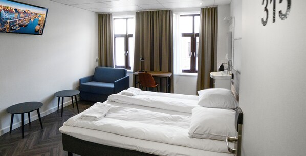 A hotel room with two beds, a desk, a chair, a TV, and a bathroom. - Go Hotel Saga (Copenhagen)