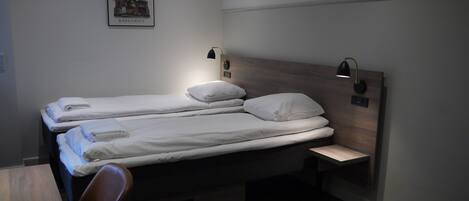 A hotel room with two single beds, a wooden headboard, bedside lamps, a small table, and a chair.