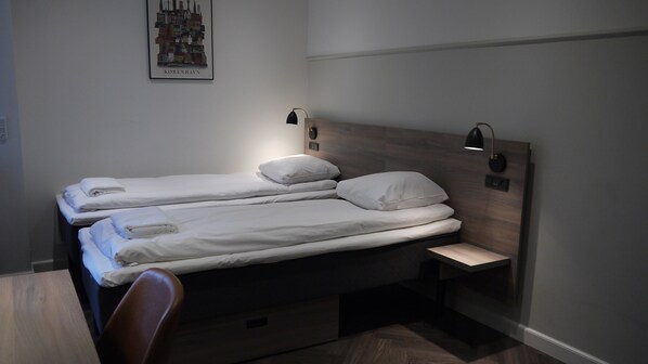 A hotel room with two single beds, a wooden headboard, bedside lamps, a small table, and a chair. - Go Hotel Saga (Copenhagen)