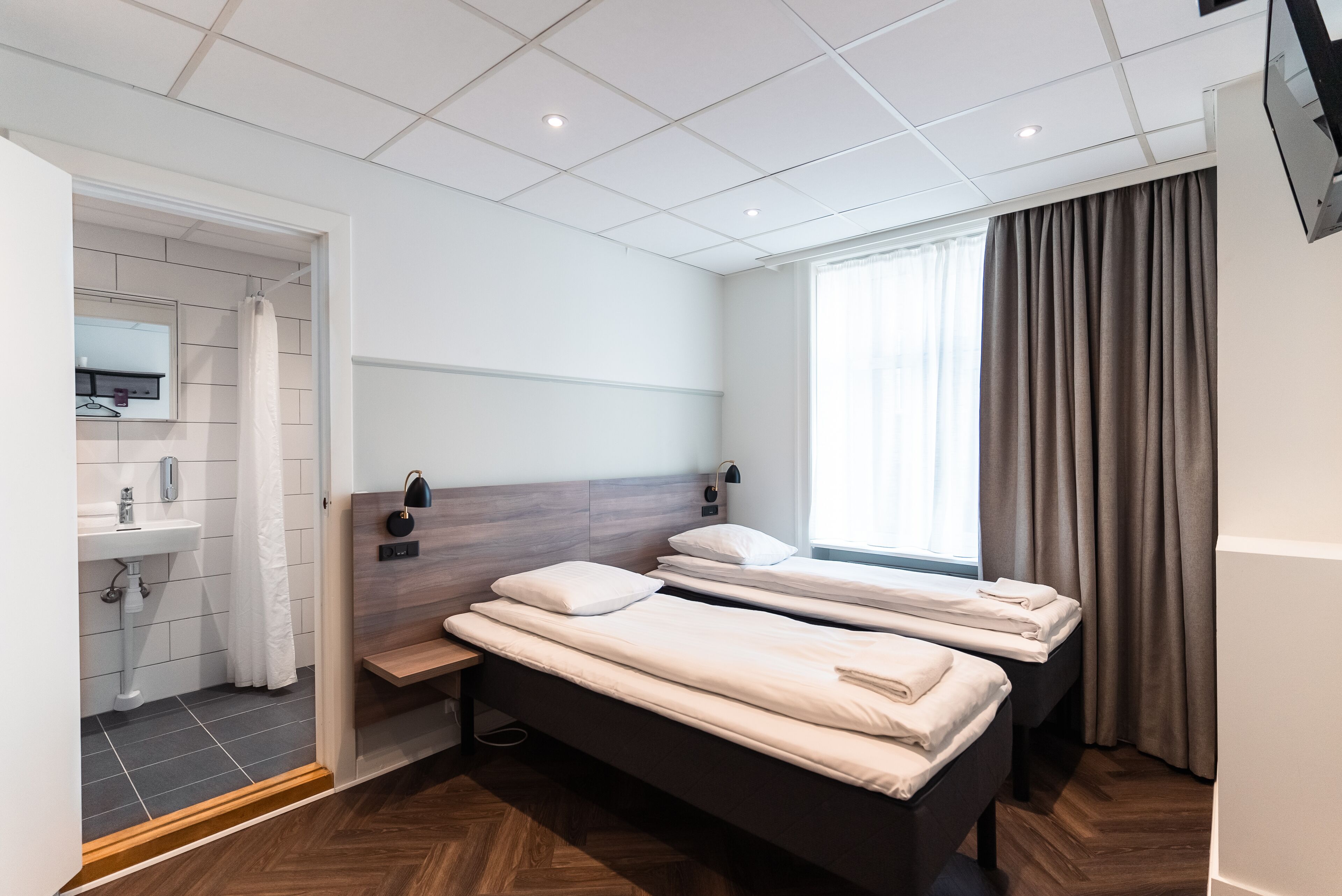 A hotel room with two beds, a sink, a mirror, and a window with curtains.