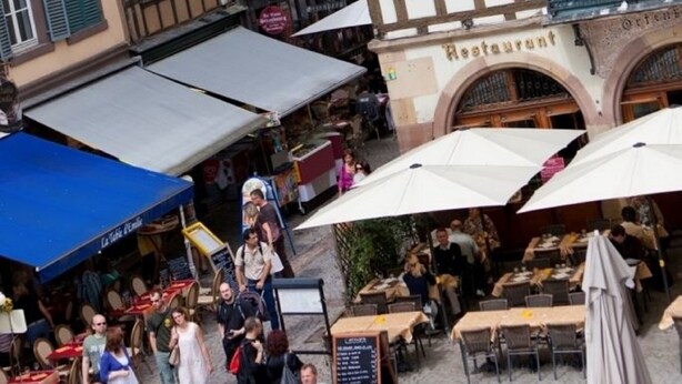 En traditionel europæisk gade med bindingsværkshuse, udendørs siddepladser og en restaurant.