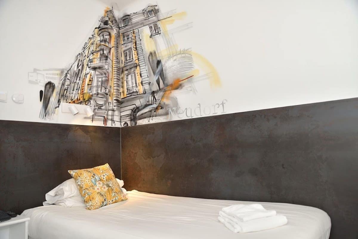 A modern hotel room with a large bed, a pillow, and a wall mural of a building.