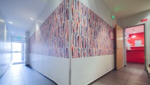 En gang med farverigt abstrakt vægkunst, et rødt reception område og et flisegulv.