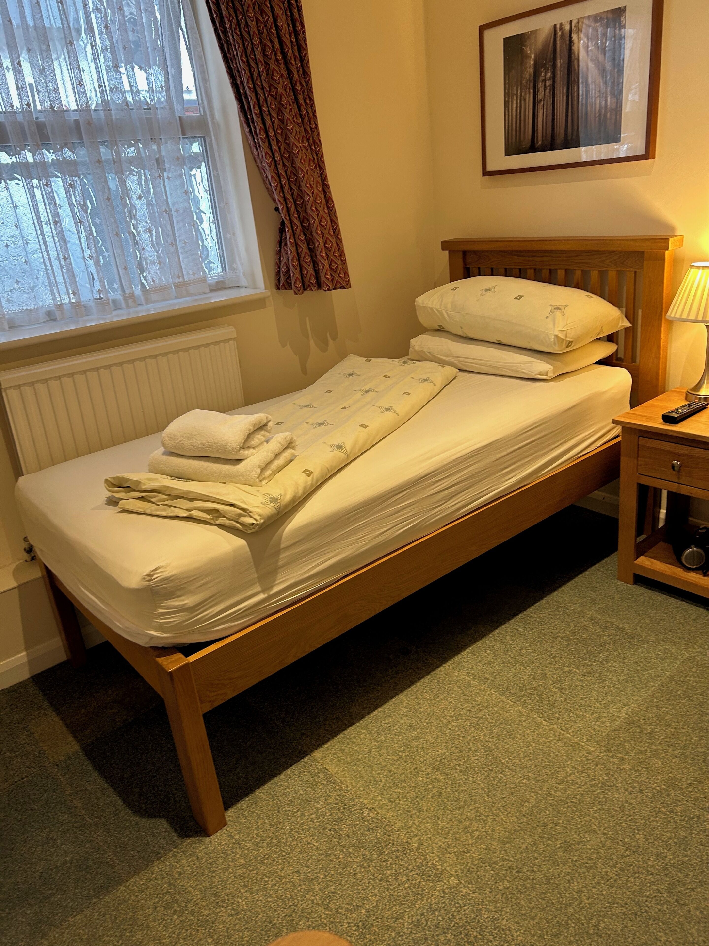 A single bed with a wooden frame, white bedding, and a bedside table with a lamp.