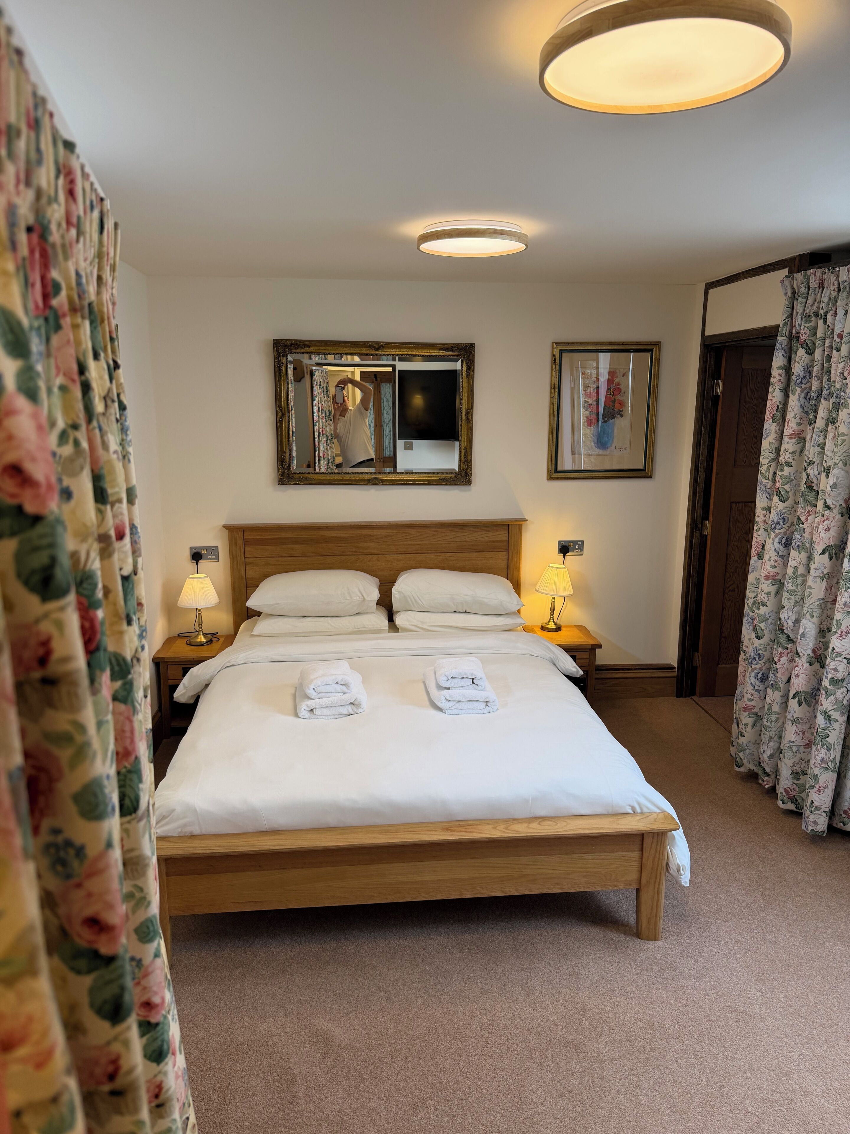 A neatly made bed with two pillows, a bedside lamp, a framed mirror, and a picture on the wall.
