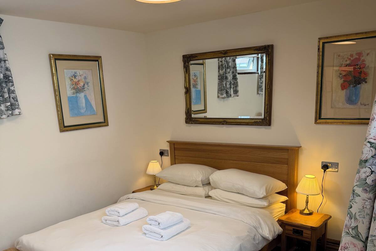 A neatly made bed with white linens and towels, a wooden headboard, bedside lamps, and framed artwork on the walls.