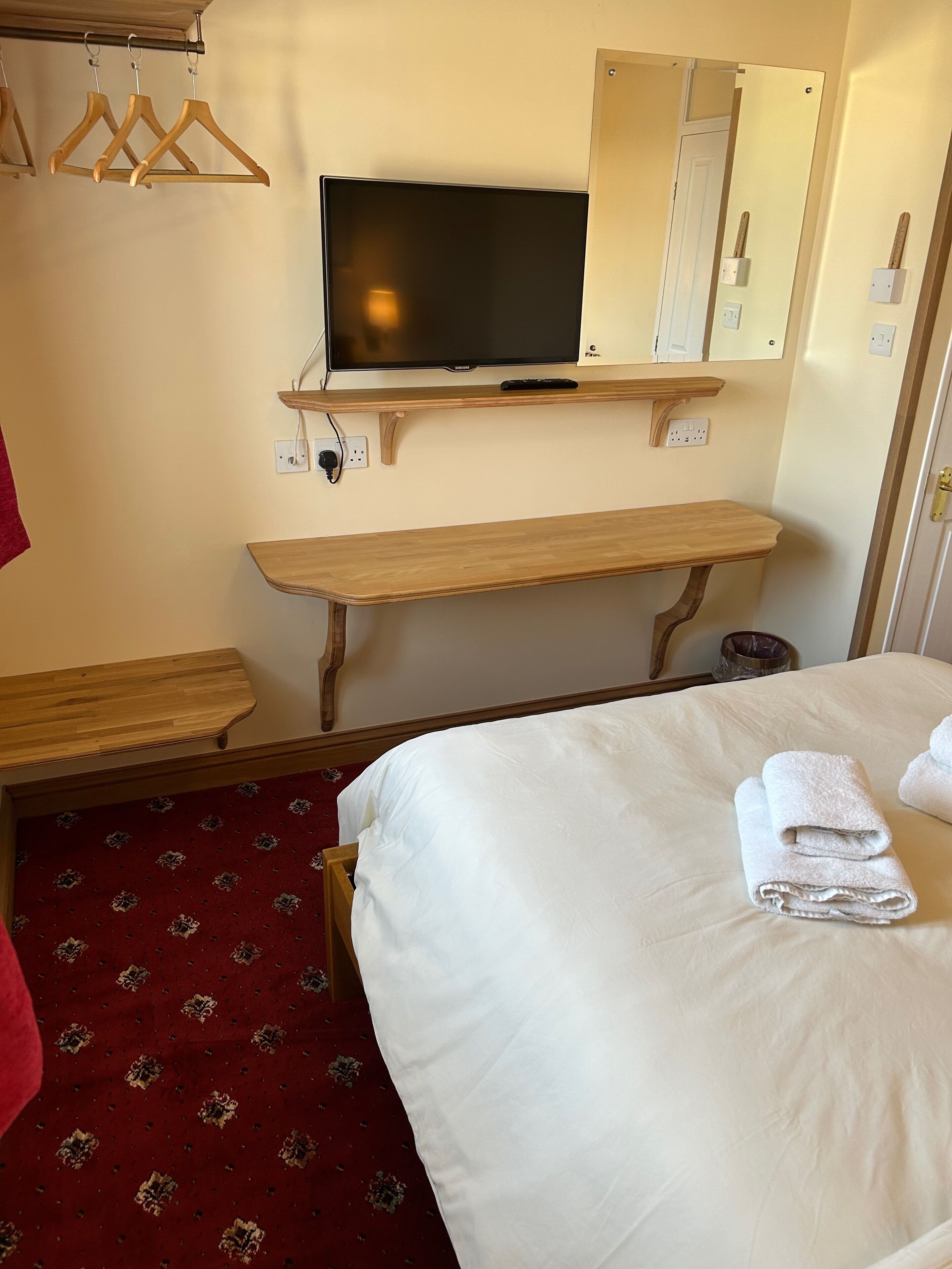 A hotel room with a bed, a wooden bench, a television, and a mirror.