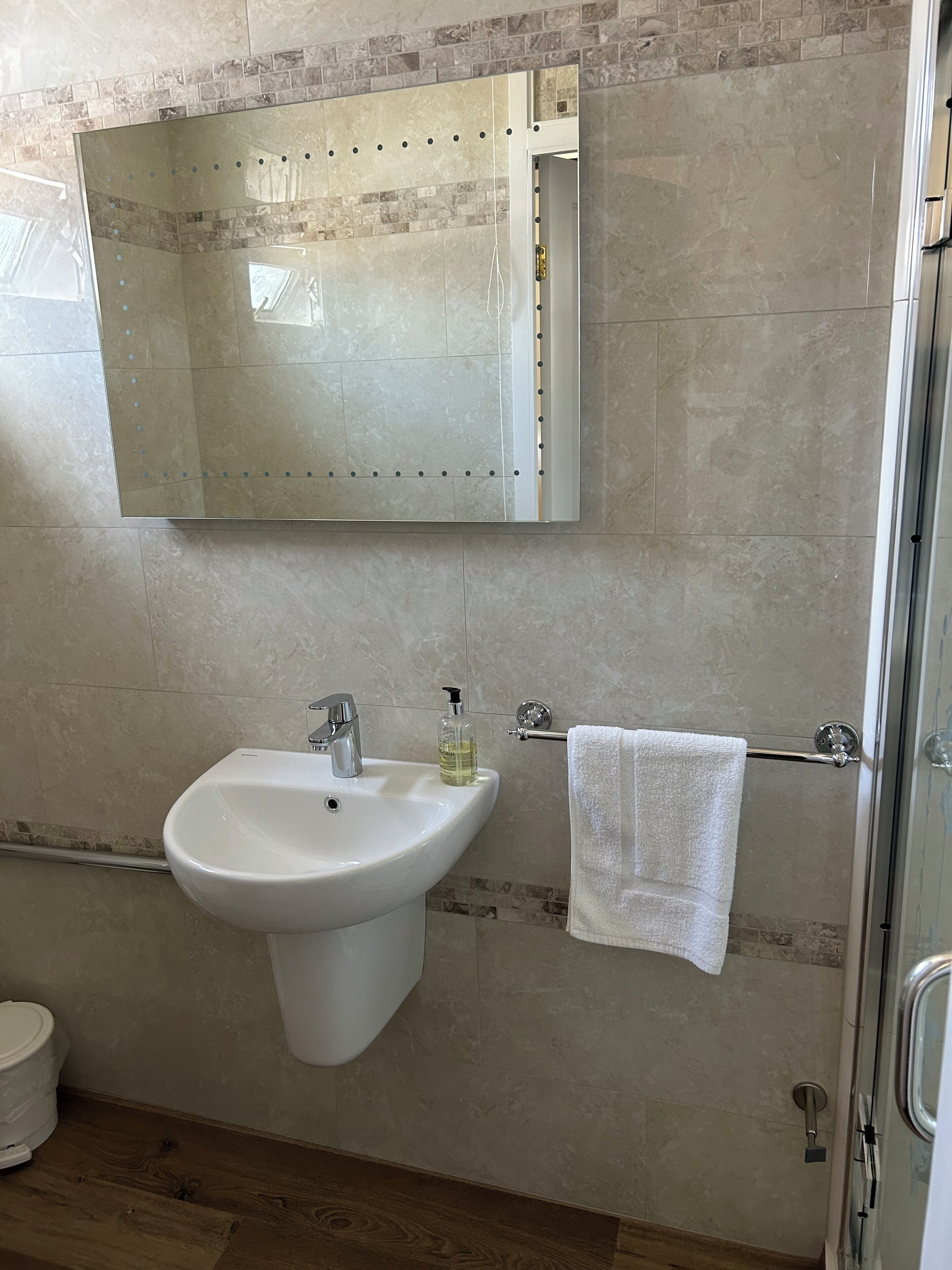 A bathroom with a white sink, a mirror, a towel rack, and a shower area.