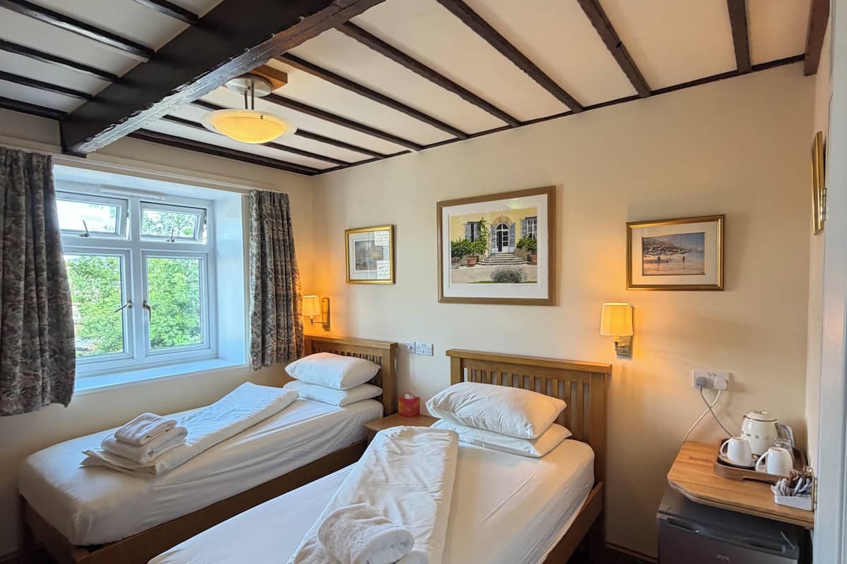 A room with two single beds, a small desk with a kettle, and a window with curtains.