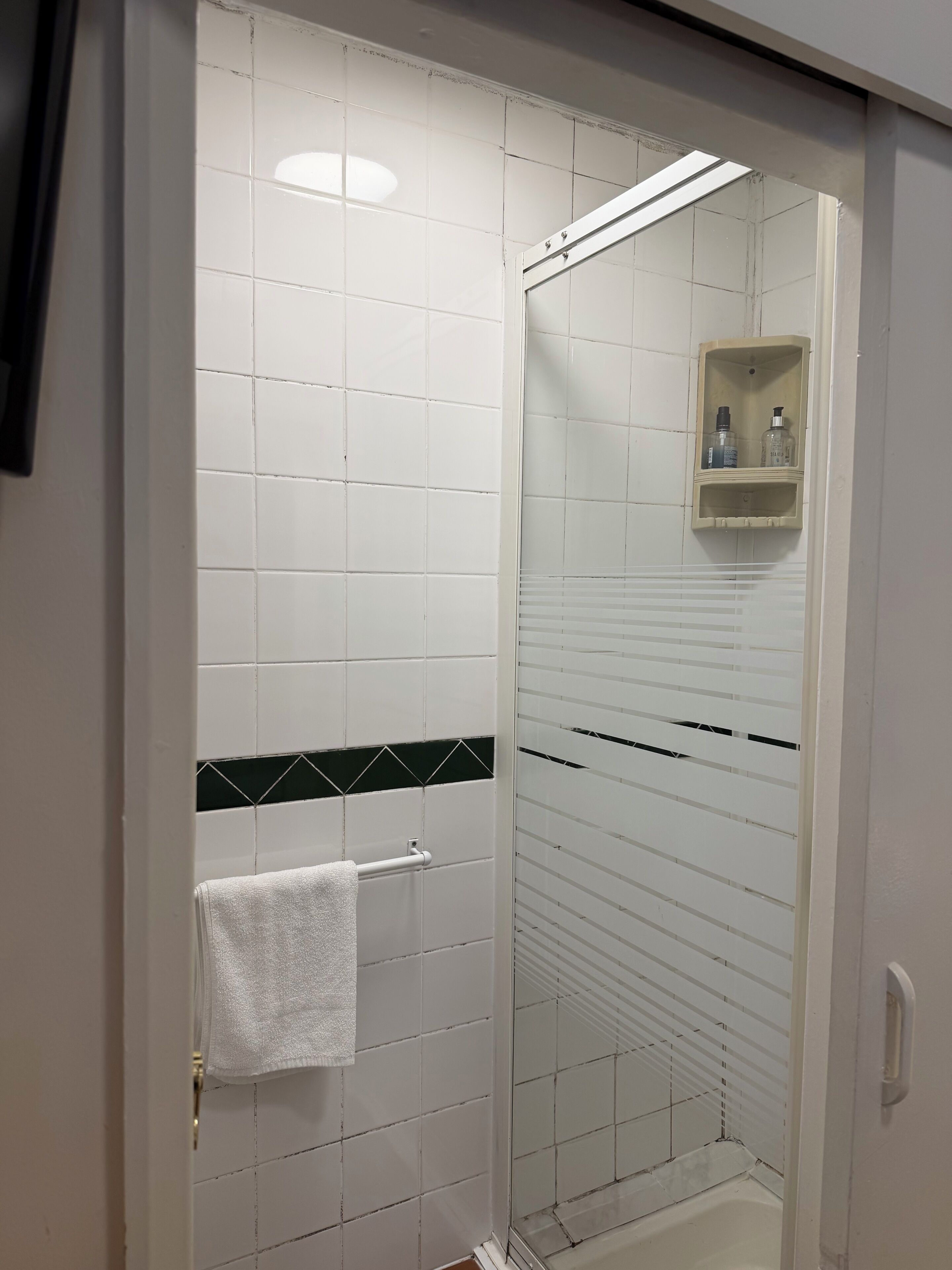 A shower with white tiles, a glass door, and a towel rack.