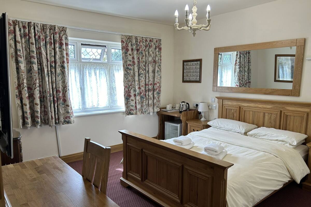 A bedroom with a wooden bed, a desk, a chair, a dresser, a chandelier, and a large mirror.