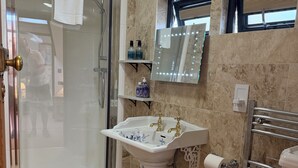 Un baño con cabina de ducha de vidrio, lavamanos pedestal, inodoro y espejo de tocador.