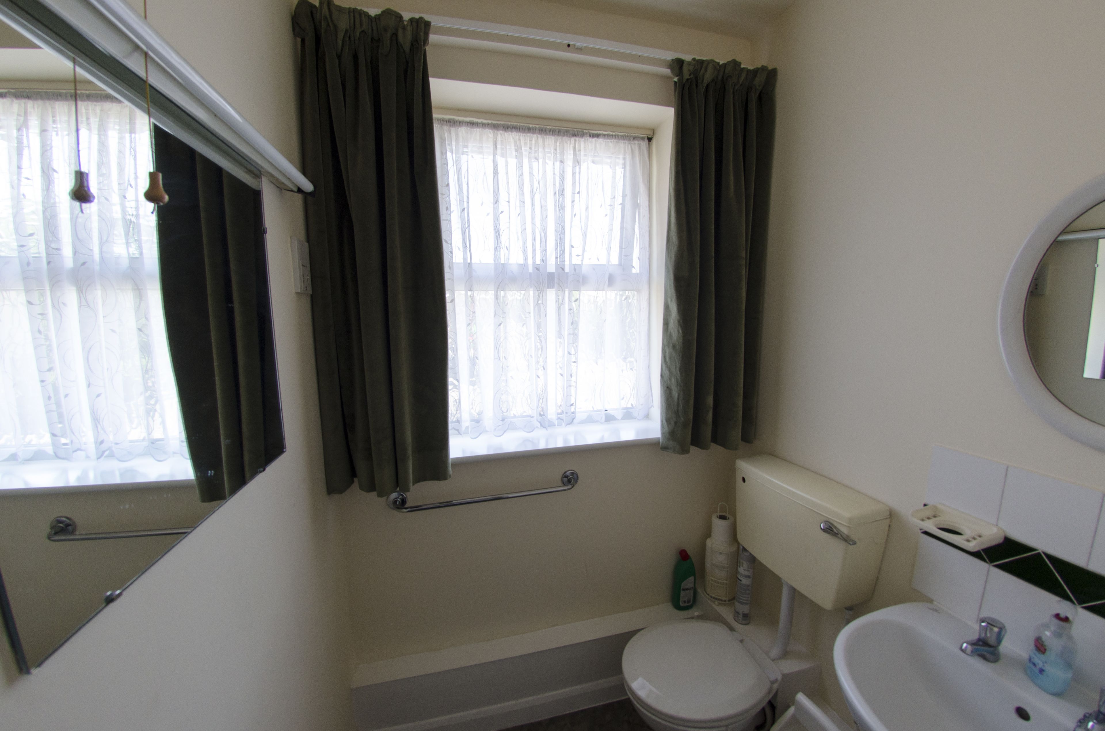 A bathroom with a toilet, sink, and window with curtains.