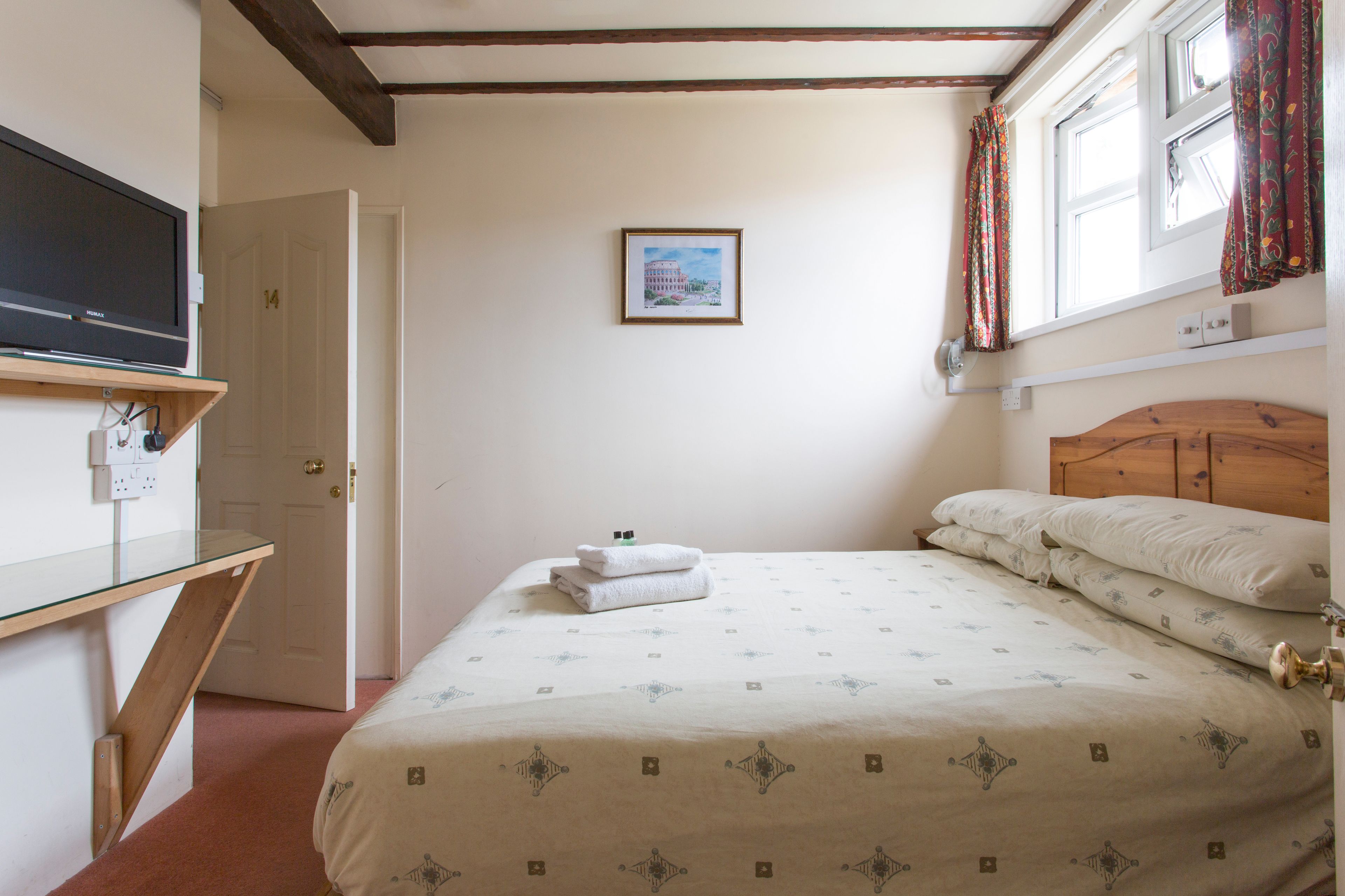 A bedroom with a bed, a television on a shelf, a door, and a framed picture on the wall.