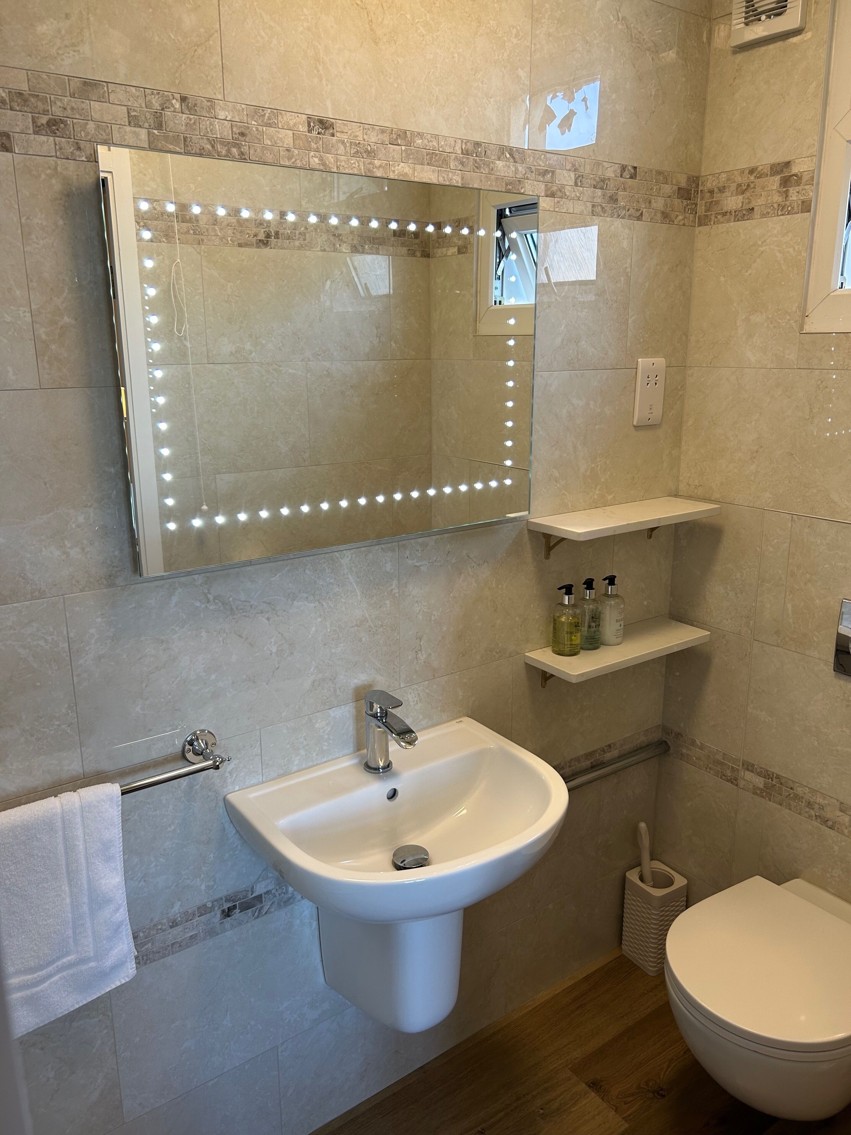 A bathroom with a vanity, sink, mirror with lights, and a toilet.