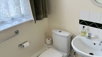 A bathroom with a toilet, bidet, sink, and window with curtains.