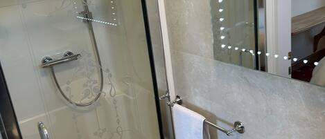A bathroom with a glass-enclosed shower, a white sink, and a mirror with lights.