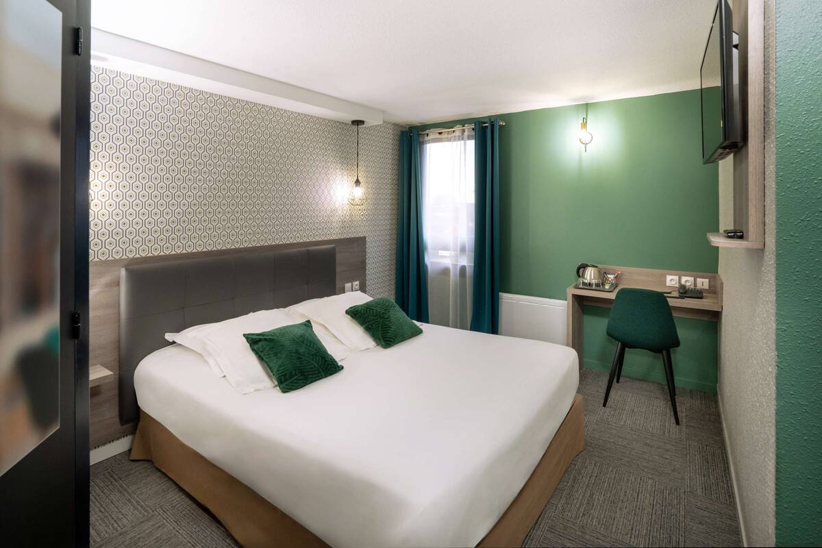A hotel room with a bed, a desk, a chair, and a TV.