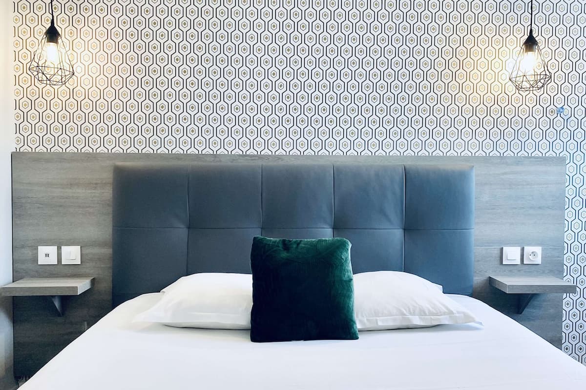 A modern hotel room with a large bed, a dark headboard, two bedside tables, and a patterned wallpaper.