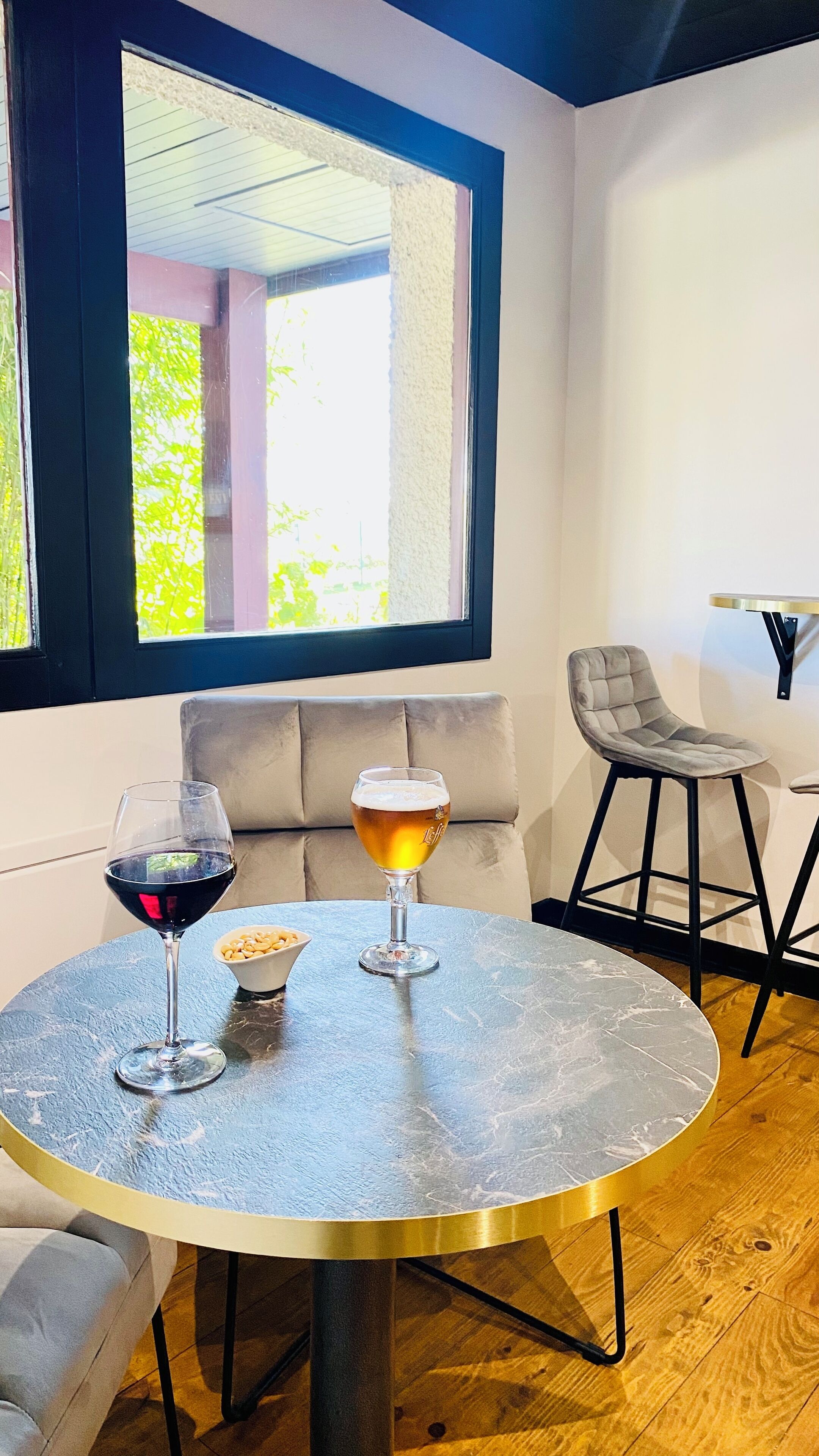 Een ronde tafel met twee bierglazen en een wijnglas, een beige bank en een stoel in een kamer met een groot raam.