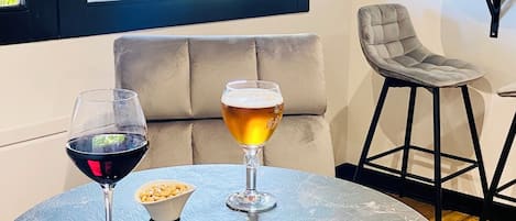 A round table with two glasses of beer and a wine glass, a beige sofa, and a chair in a room with a large window.