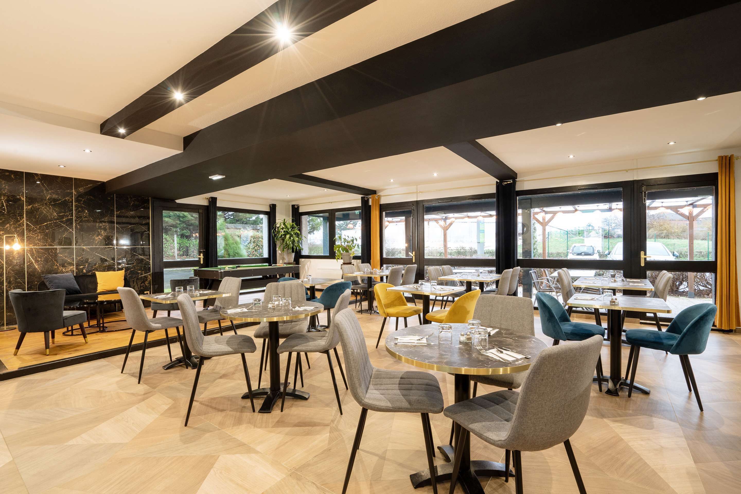 A modern restaurant with a mix of round and rectangular tables, upholstered chairs in various colors, and a marble wall with a black and gold pattern.
