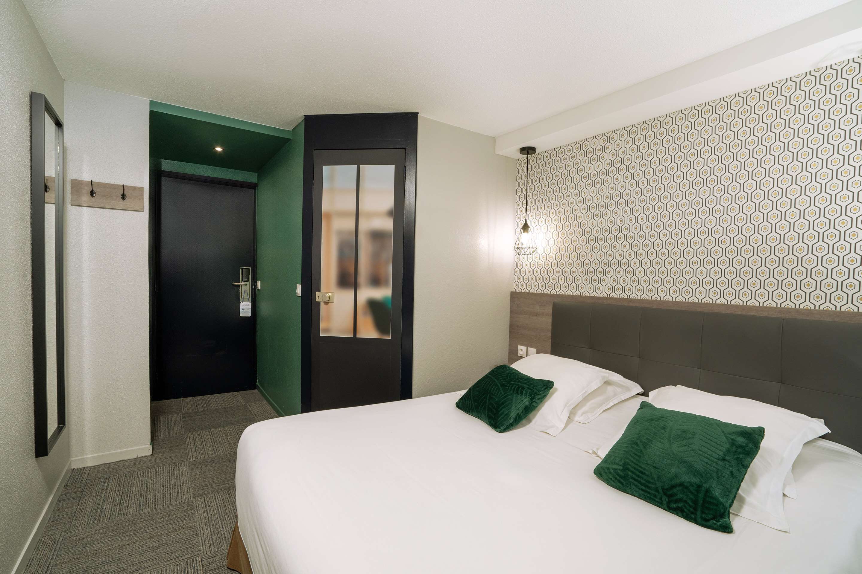 Habitación de hotel con cama, dos almohadas, una puerta y un papel tapiz estampado.