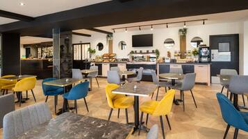 A modern restaurant with marble tables and colorful chairs, a kitchen area, and a flat-screen TV on the wall.