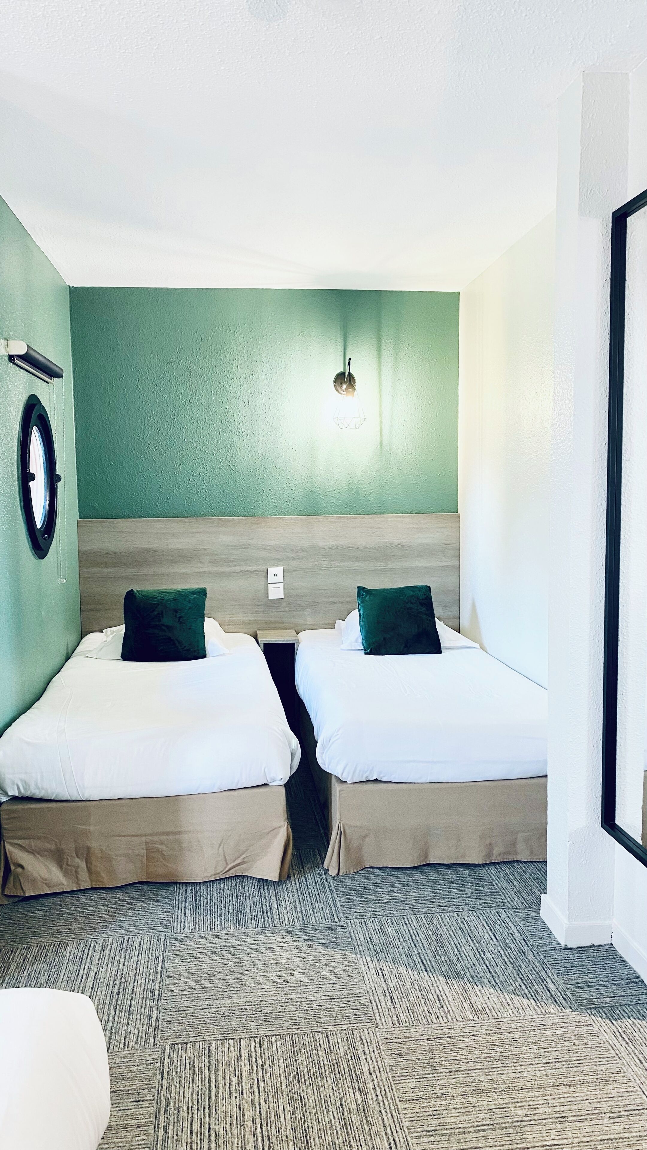 A room with two beds, a headboard, a wall-mounted light fixture, and a carpeted floor.