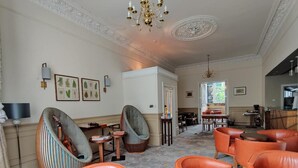 A spacious lounge area with leather armchairs, a piano, and a dining table.