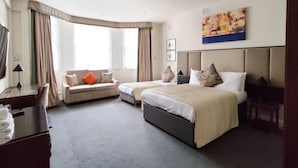 A hotel room with a sofa, two beds, a desk, and a large window.