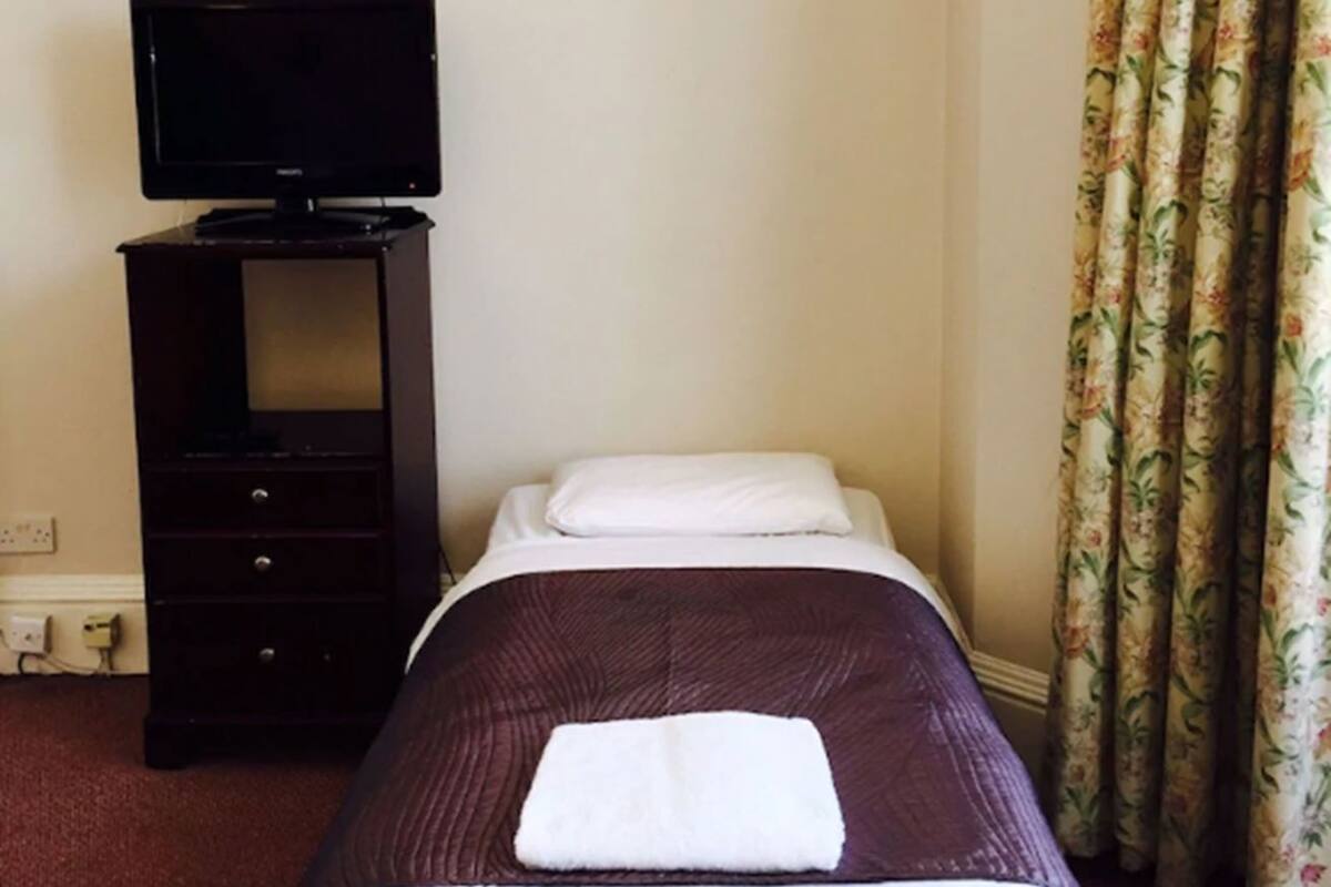 A hotel room with a bed, a TV on a stand, a dresser, and a curtain.