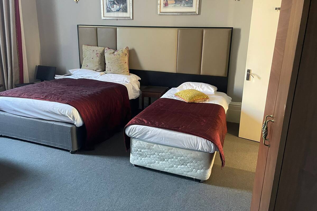A hotel room with two beds, a headboard, a nightstand, and a door.
