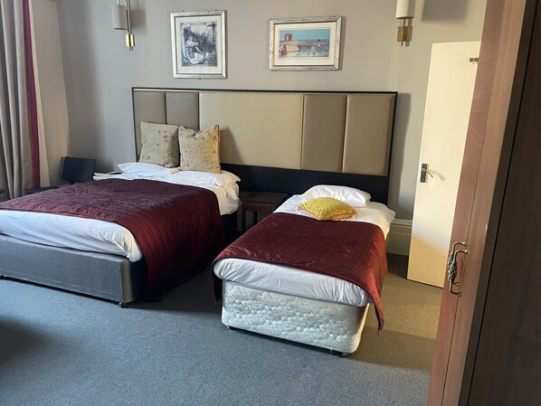 A hotel room with two beds, a headboard, a nightstand, and a door. - Blue Bells (London)