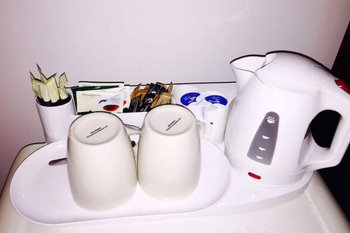 A coffee maker, two cups, and a kettle on a countertop.
