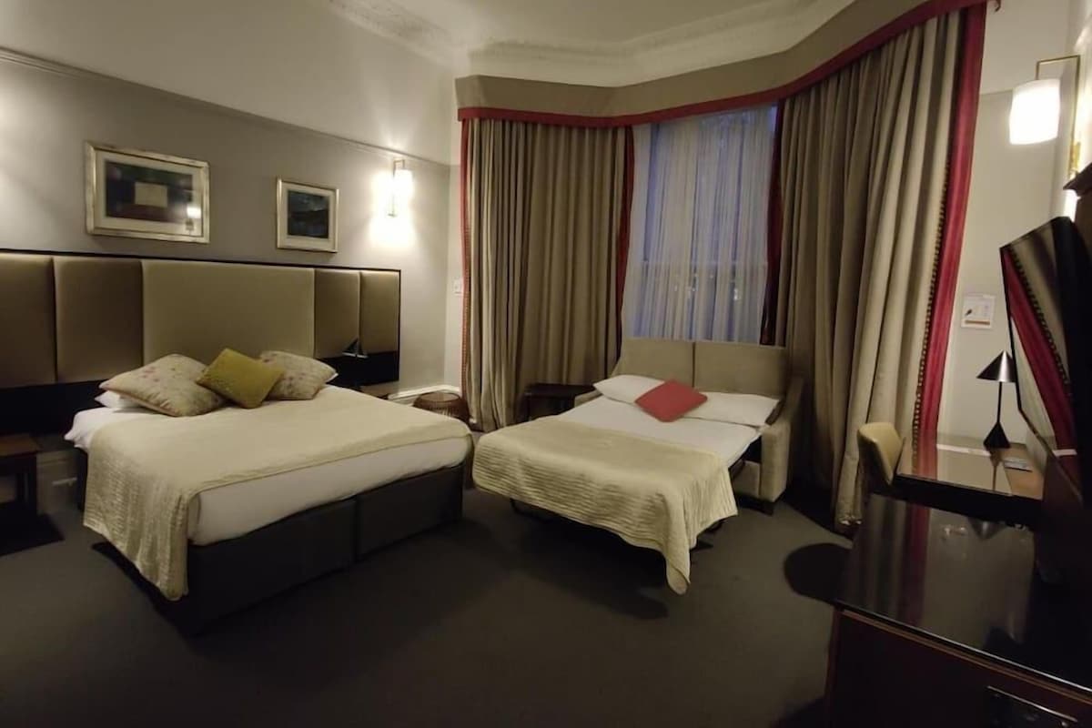 A hotel room with two beds, a flat-screen TV, a desk, and a window with curtains.