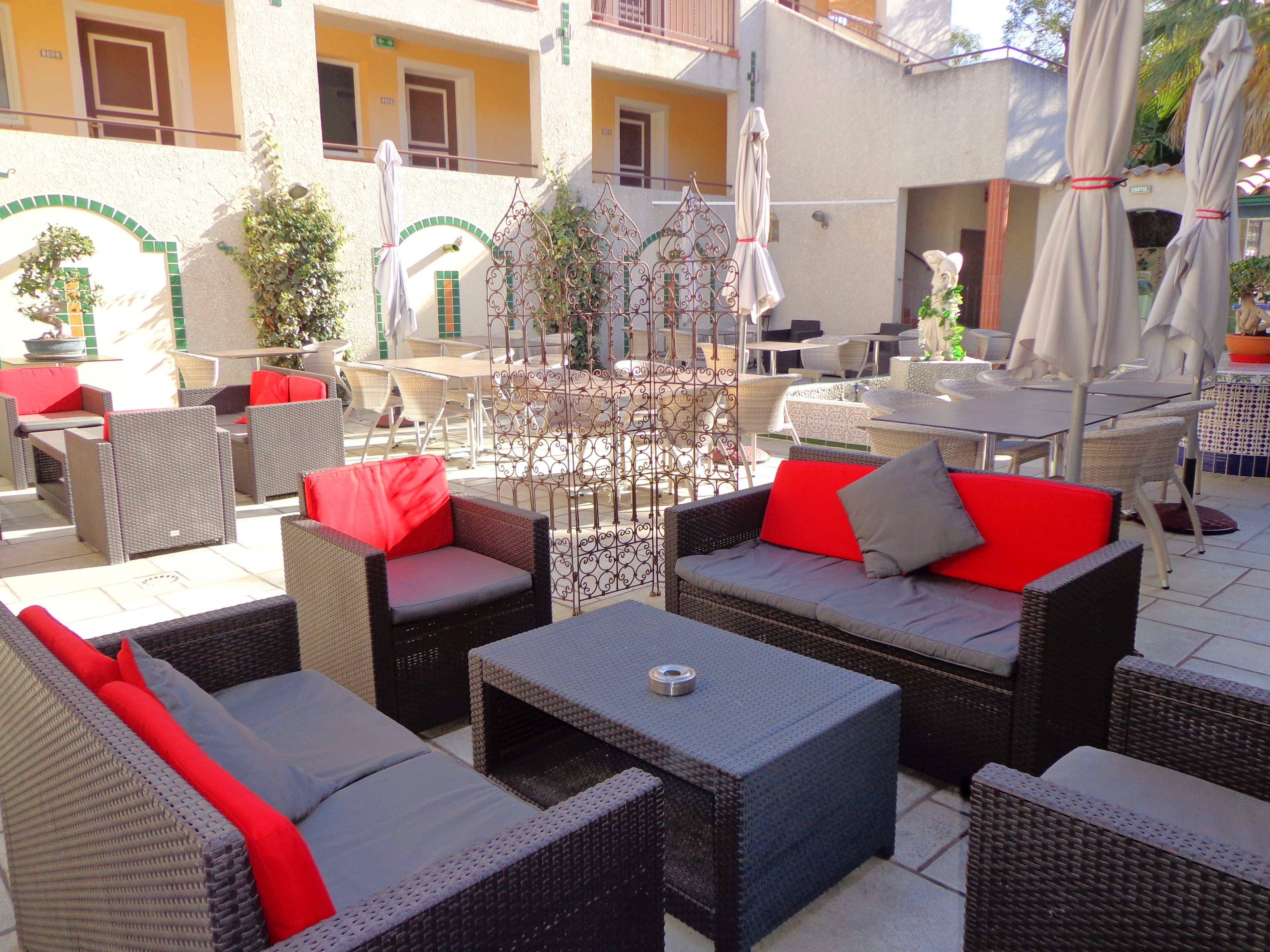 An outdoor patio area with wicker furniture, red cushions, and umbrellas.