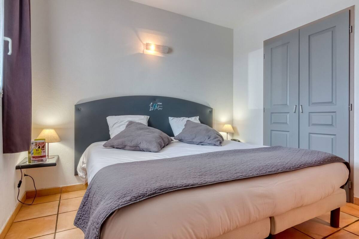 A hotel room with a bed, two bedside lamps, a nightstand, a wardrobe, and a wall-mounted light fixture.