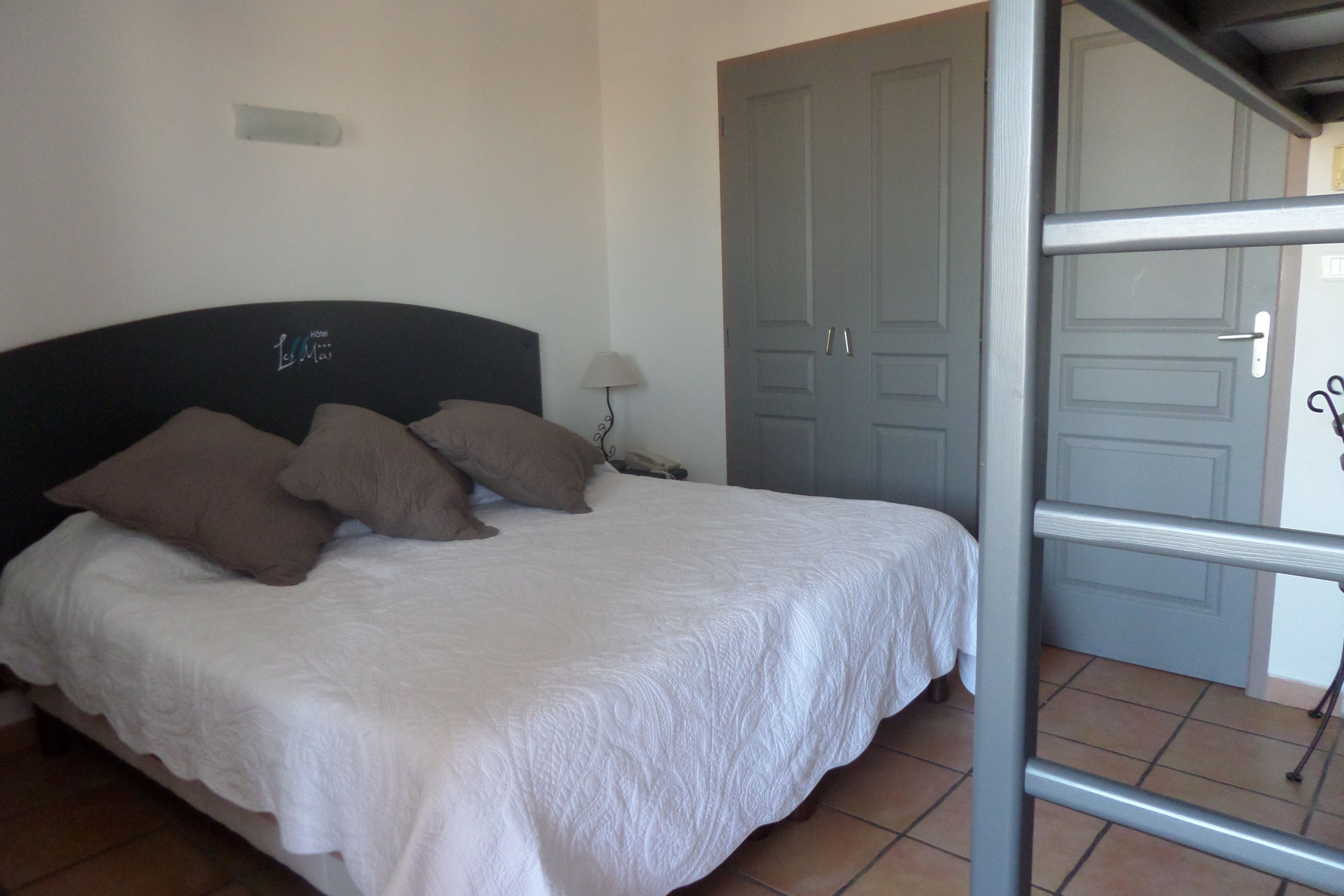 A bed with a white bedspread and several pillows, a nightstand with a lamp, and a door in the background.