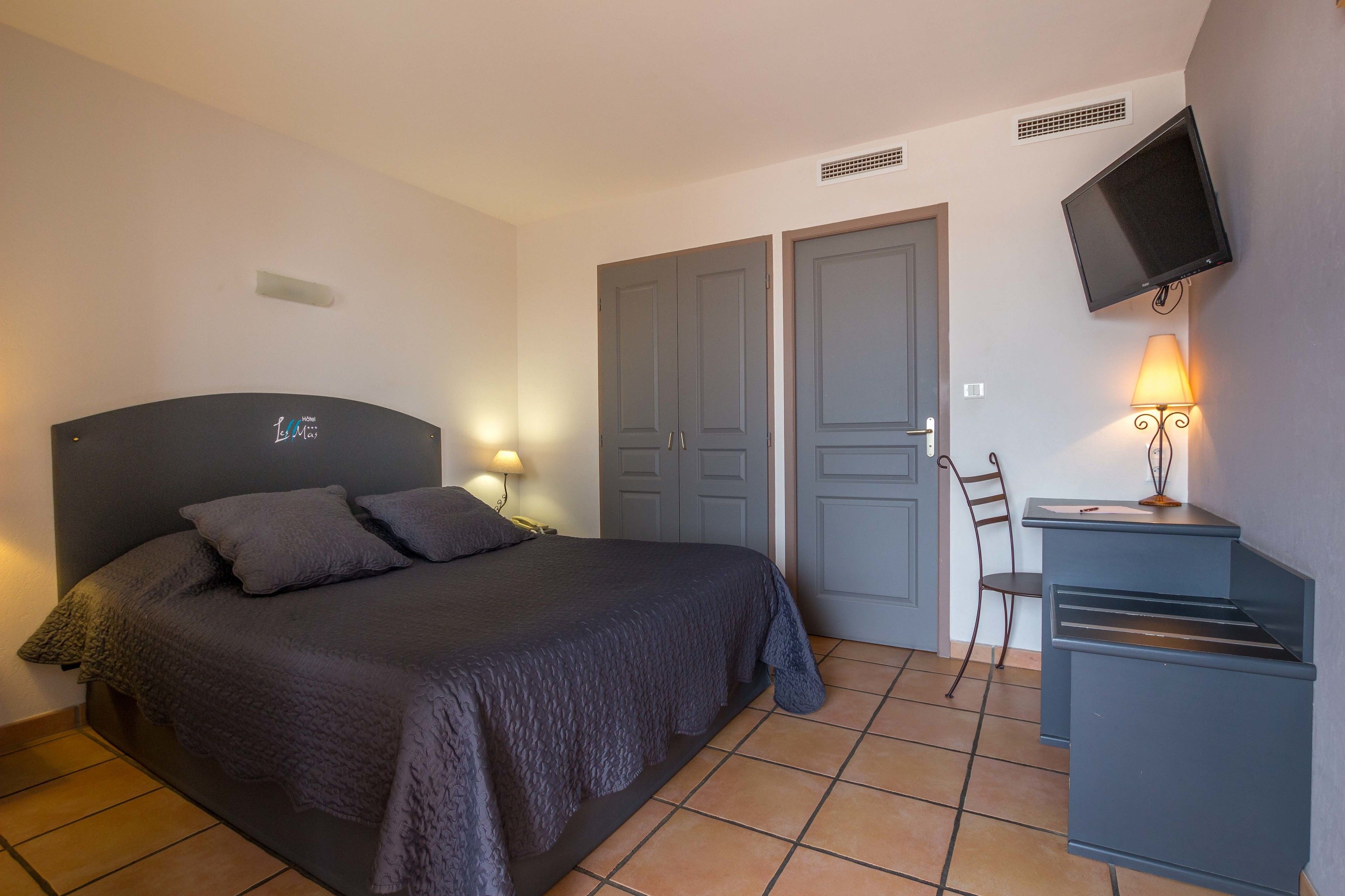 A bedroom with a bed, a desk, a chair, a TV, and a lamp.