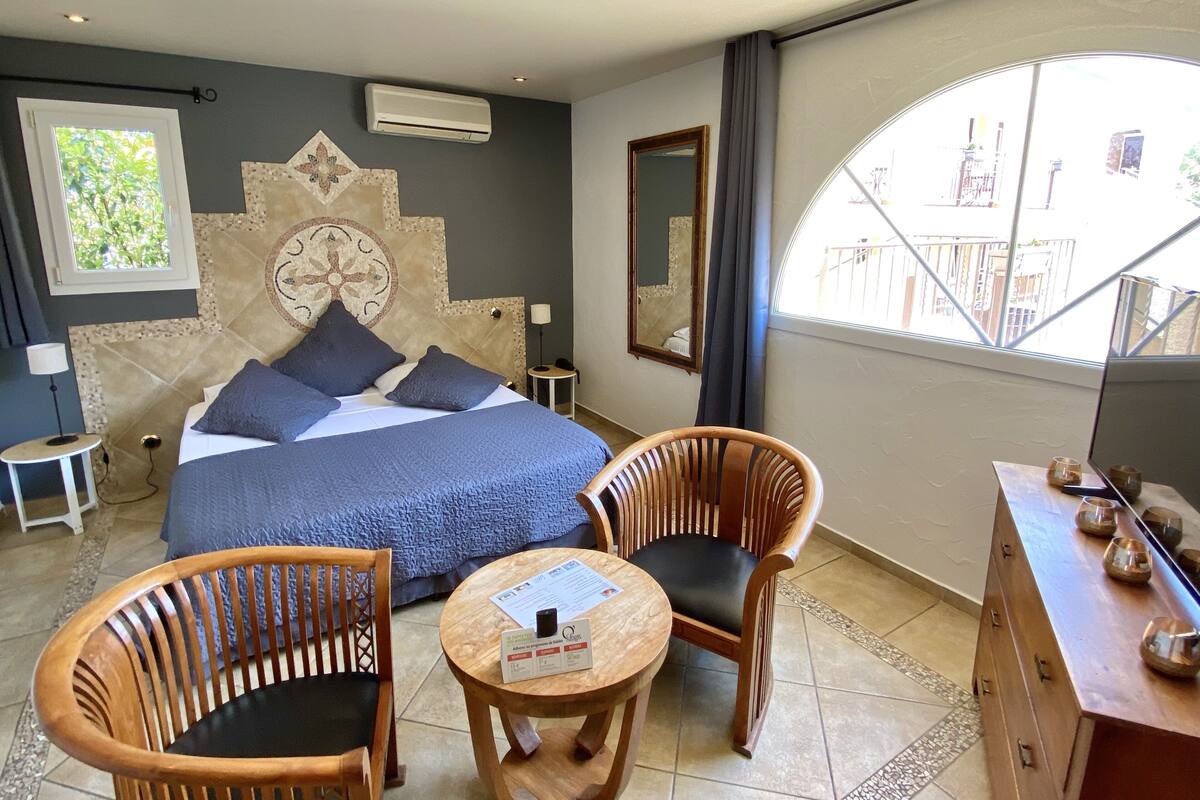A hotel room with a large bed, two wooden chairs, a small table, a dresser, and a balcony with a railing.