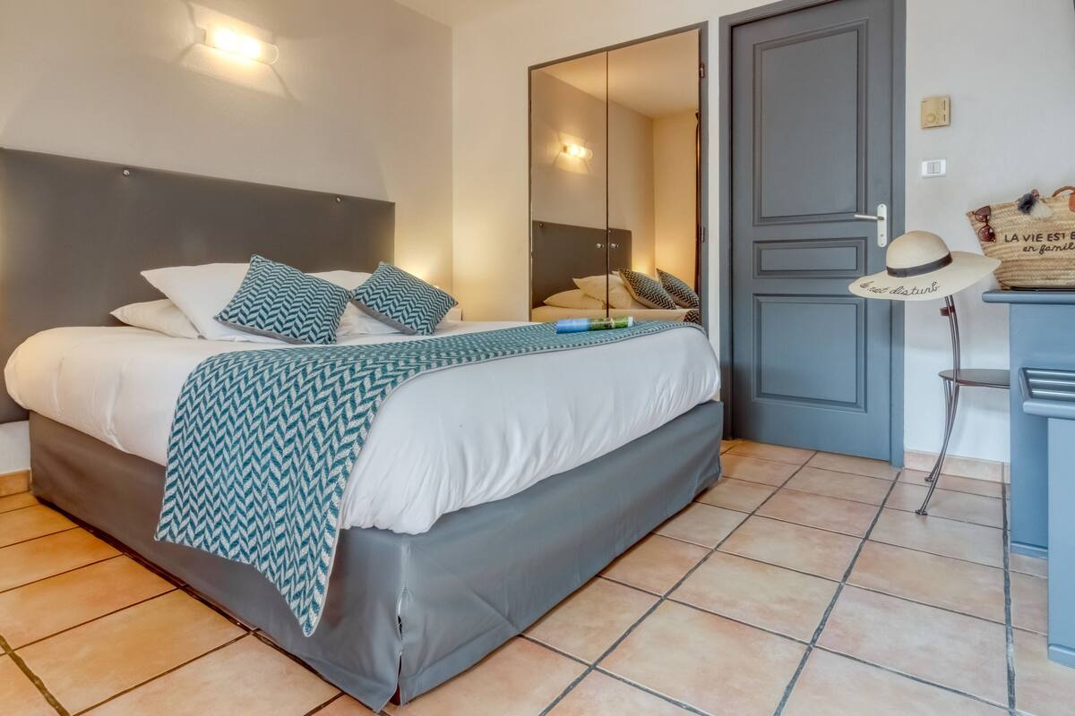 A neatly made bed with a patterned throw, a bedside table with a lamp, and a door with a mirror.