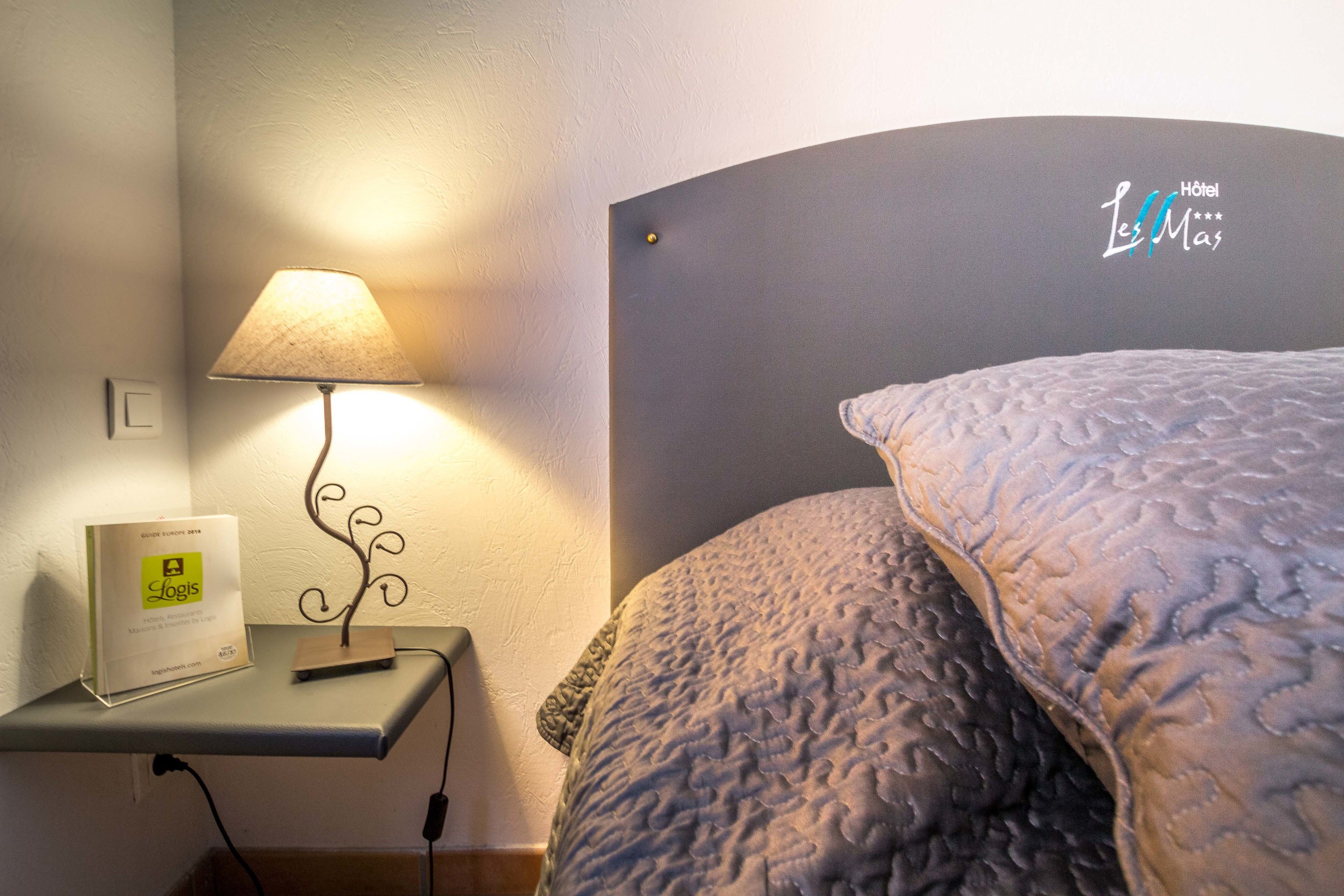 Un dormitorio con cama, mesita de noche con lámpara, y un cartel que indica el nombre del hotel.
