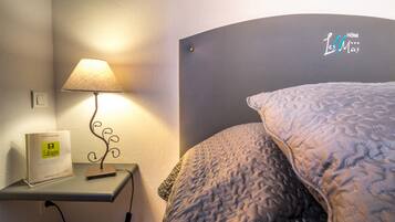 Un dormitorio con cama, mesita de noche con lámpara, y un cartel que indica el nombre del hotel.
