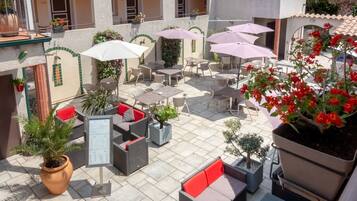 An outdoor patio with multiple seating areas, umbrellas, and potted plants.