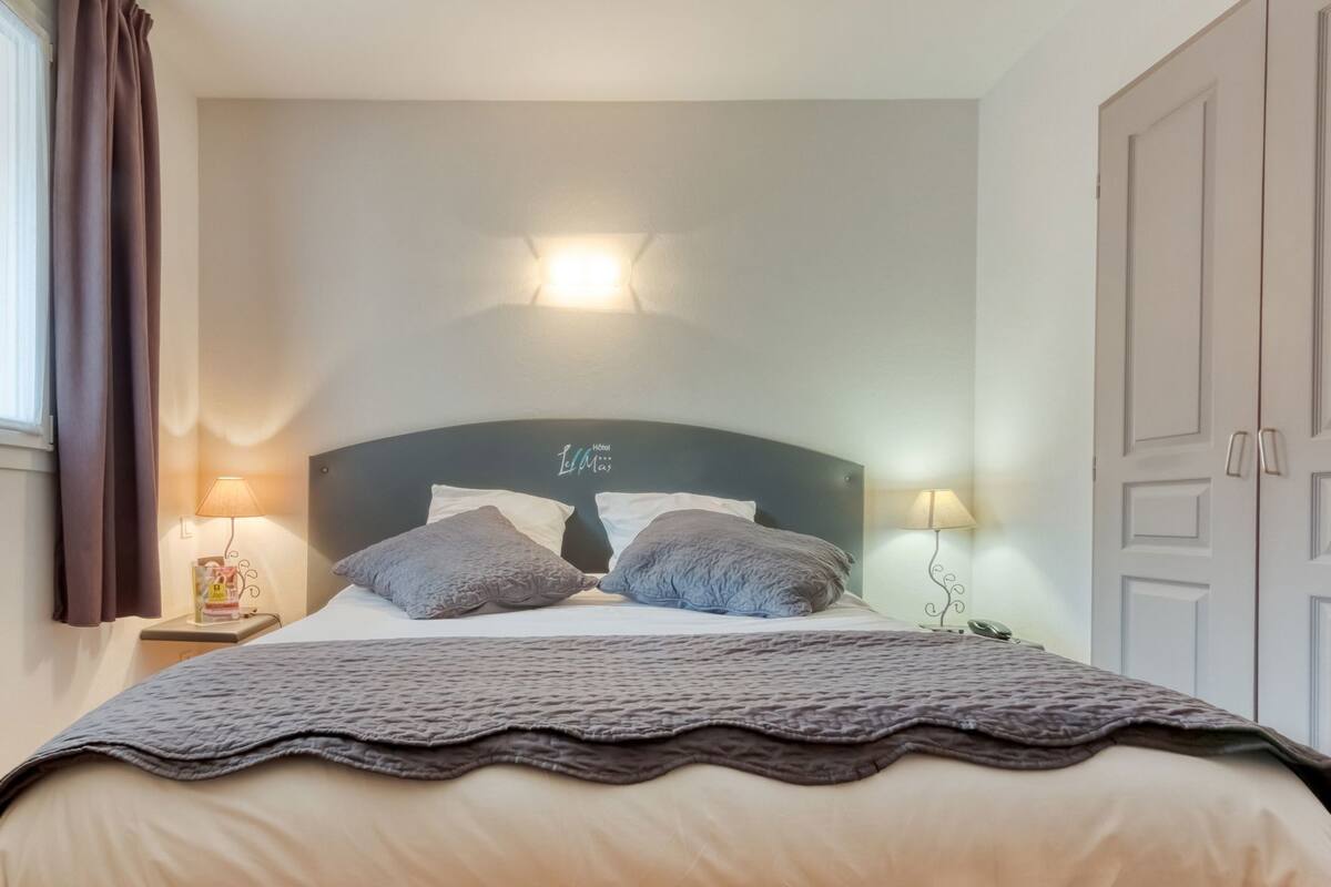 A hotel room with a bed, two bedside lamps, a headboard with a light fixture, and a wardrobe.