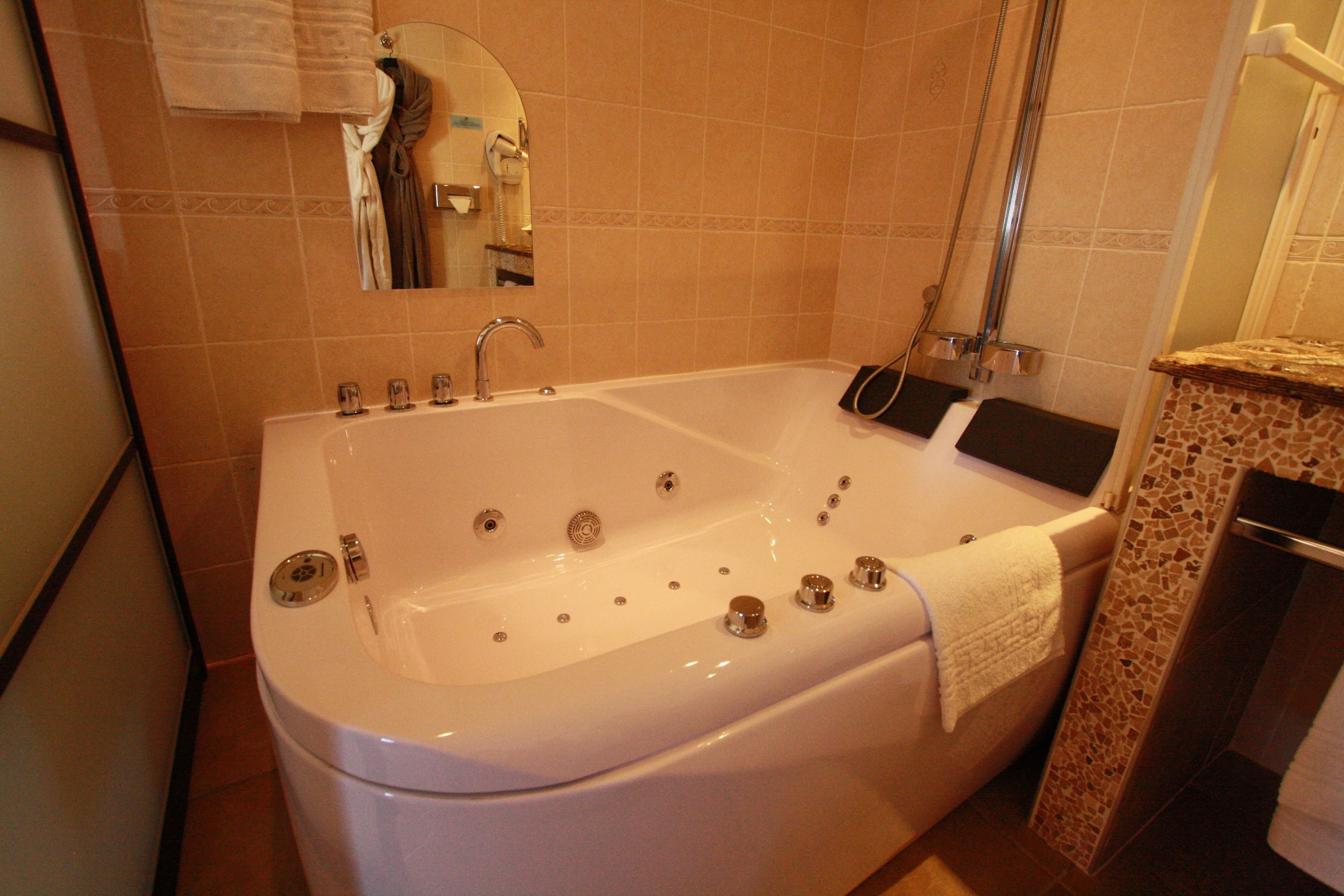 A large white bathtub with multiple jets, a handheld showerhead, and a towel rack.