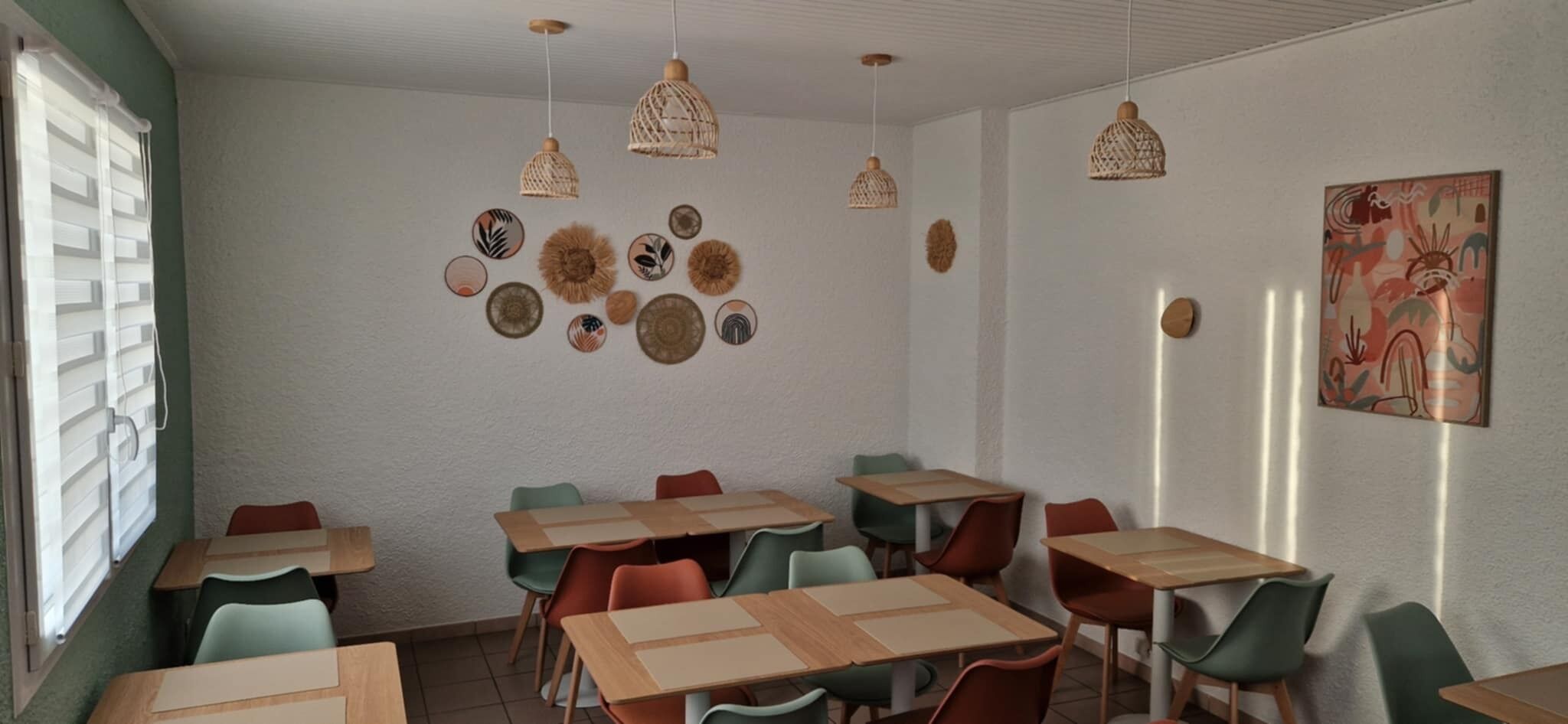 A room with multiple tables and chairs, a wall decorated with various circular and oval wall hangings, and a painting on the right wall.