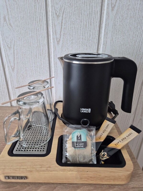 A black electric kettle with a transparent glass carafe and a tea infuser on a wooden tray.